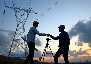 Silhouetted men shaking hands in a sunset, survey tripod in the background