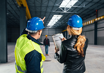 Man and woman wearing hardhats, standing in a partially-constructed building