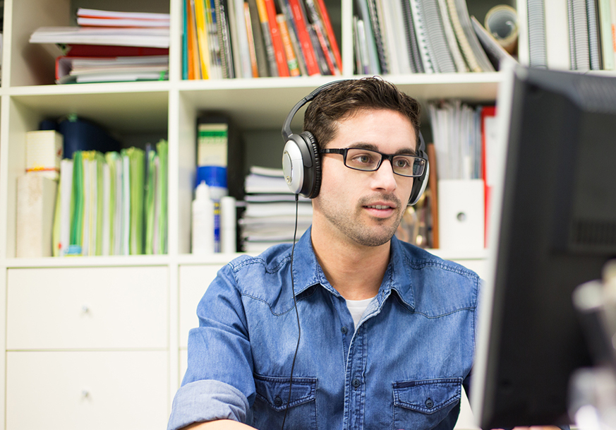 Man looking at computer, wearing headphones & talking on phone
